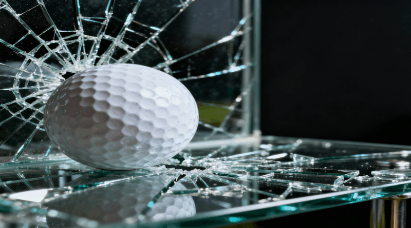 Golfball zerbricht Glasscheibe mit Rissen und Splittern
